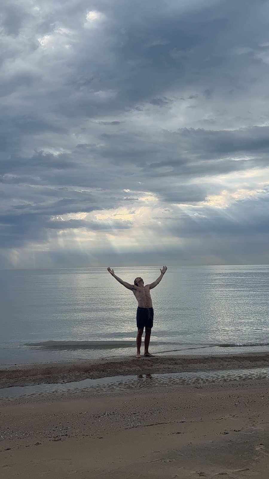 The coach on the beach with arms raised to the sky as sun rays break through the clouds